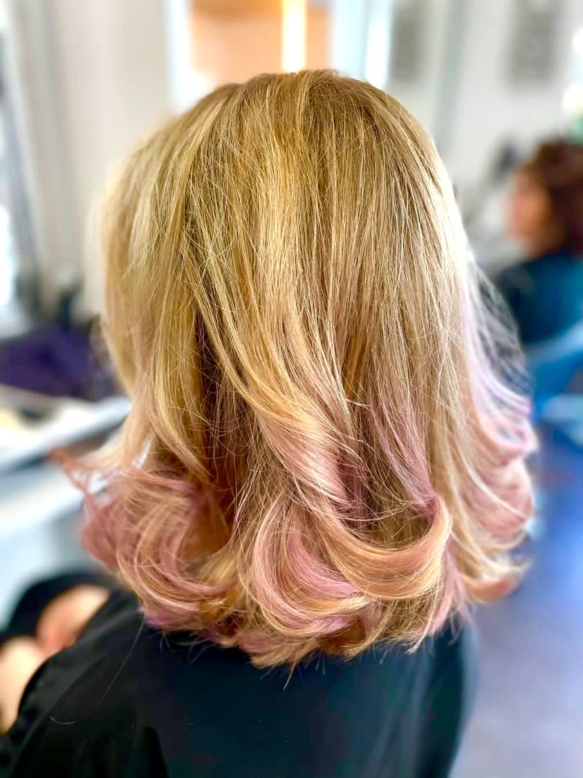 Cheveux de femme, crêpés et dégradés, avec des racines blondes se fondant dans des pointes roses. Dans un salon de coiffure.