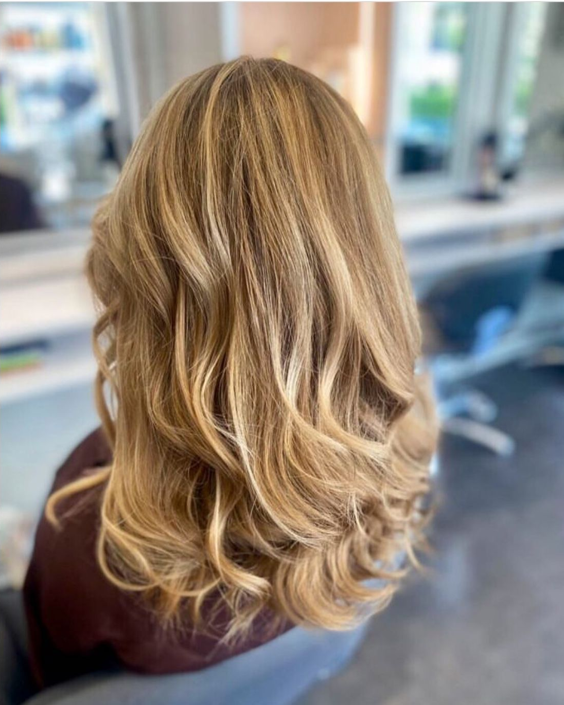 Femme aux longs cheveux blonds ondulés, coiffée en salon, mettant en valeur des mèches.
