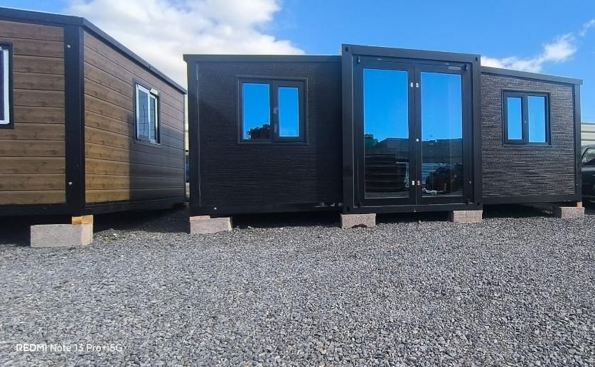 Casas pequeñas modernas con revestimiento de madera oscura en un terreno de grava, con un coche aparcado entre ellas.