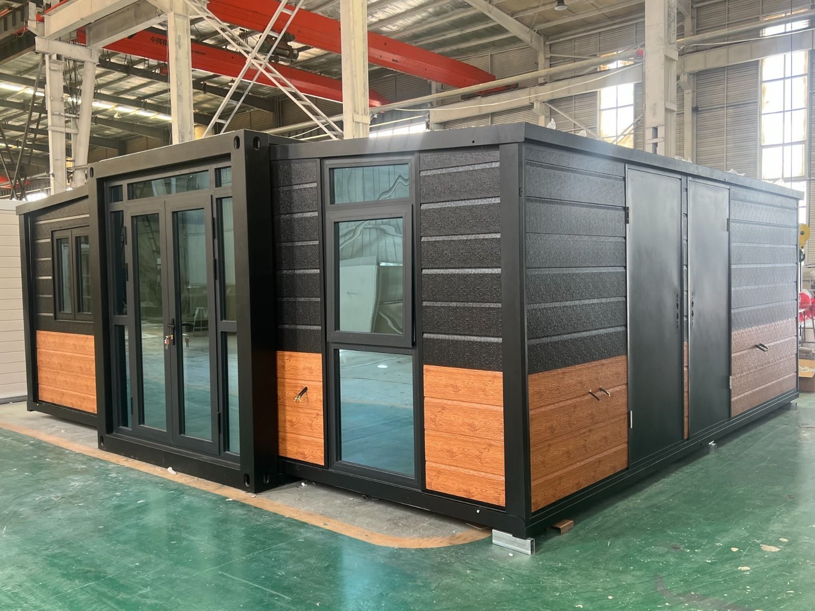 Exposición de una habitación modular prefabricada en negro y madera dentro de una sala de exposiciones de un almacén.