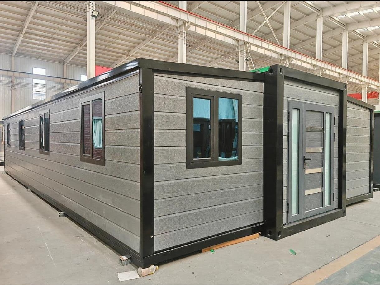 Edificio modular gris con detalles en negro y grandes ventanales dentro de un almacén industrial.
