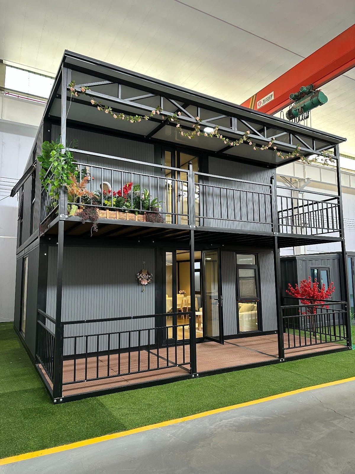 Minicasa moderna de dos plantas de metal negro con balcones, puertas de cristal y plantas expuestas en el interior.