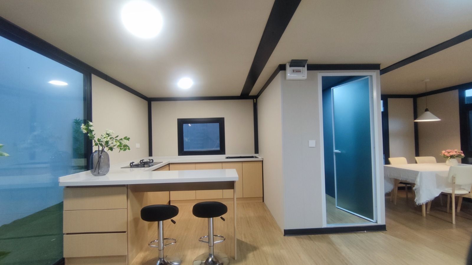 Cocina moderna con barra tipo isla, ventana grande y puerta abierta a un comedor iluminado.