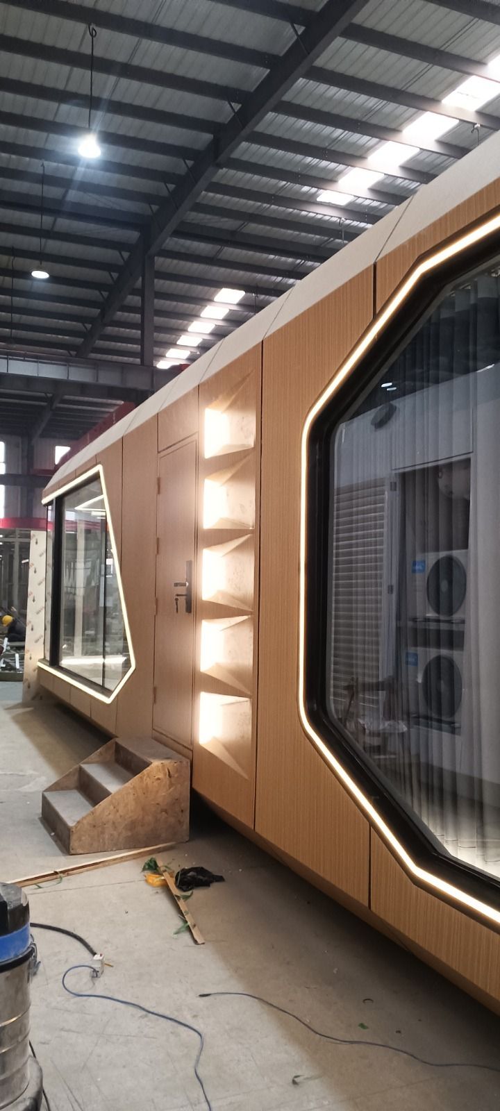 Exterior de un edificio modular en construcción dentro de un almacén, con revestimiento de madera y grandes ventanales.