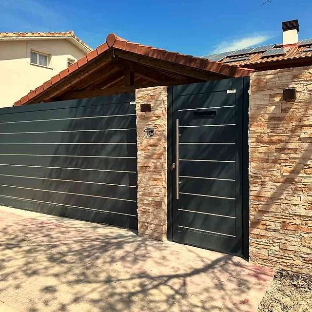 Una puerta negra está al lado de una pared de ladrillos y una casa.