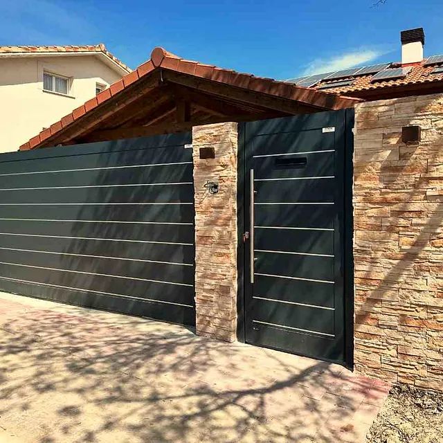 Una puerta negra está junto a una pared de ladrillos frente a una casa.