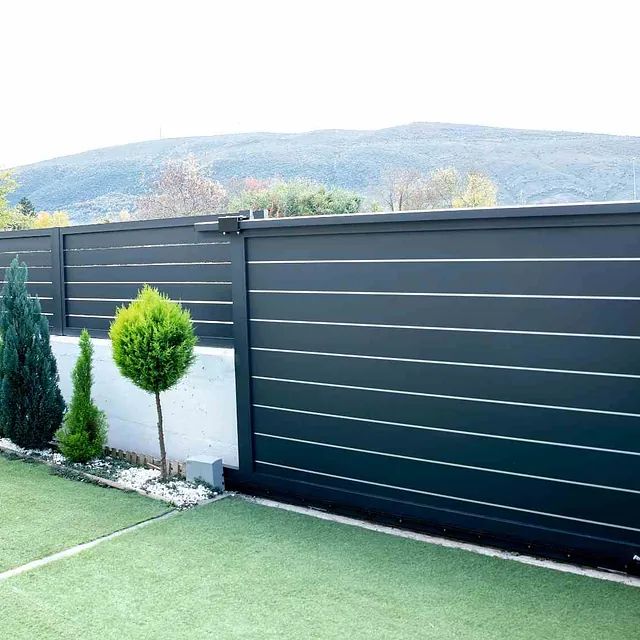 Una valla negra con una puerta corrediza y árboles delante de ella.