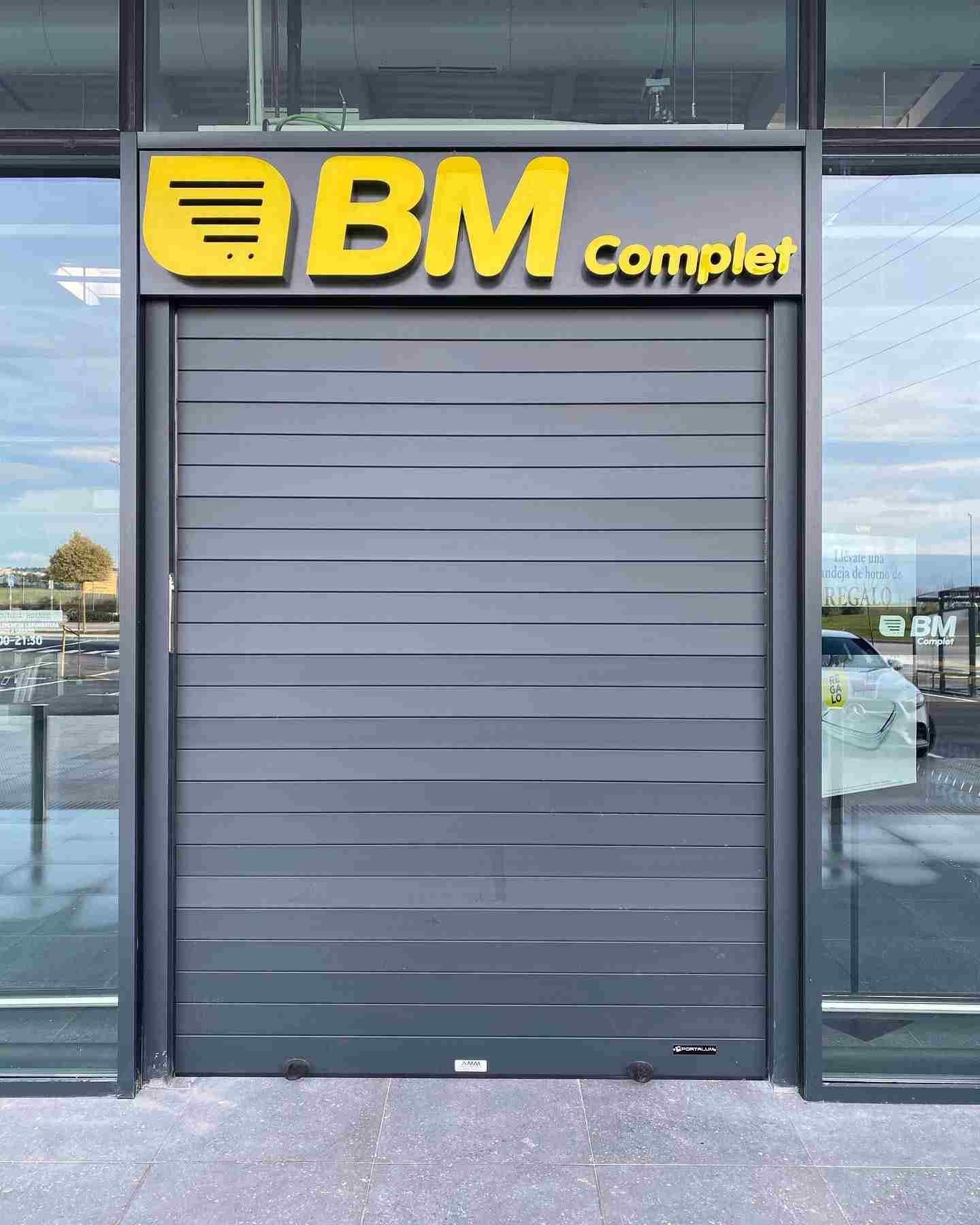 Una puerta enrollable negra con un cartel amarillo encima que dice bm complet.
