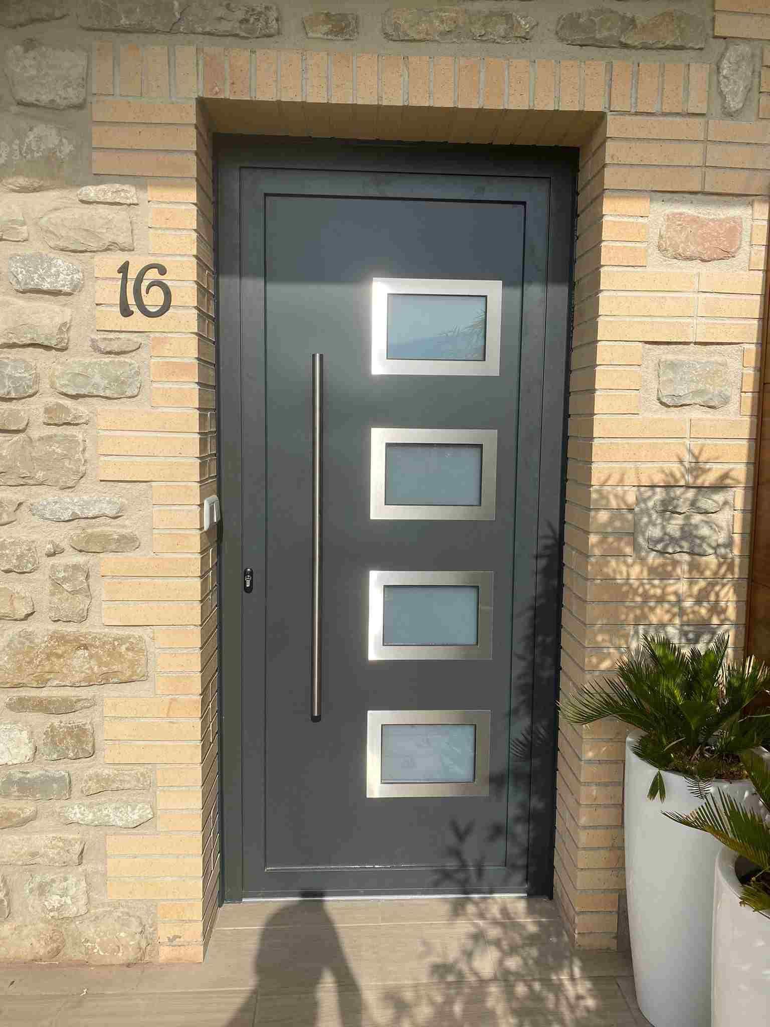 Una puerta negra con manija de acero inoxidable está en una pared de ladrillos.