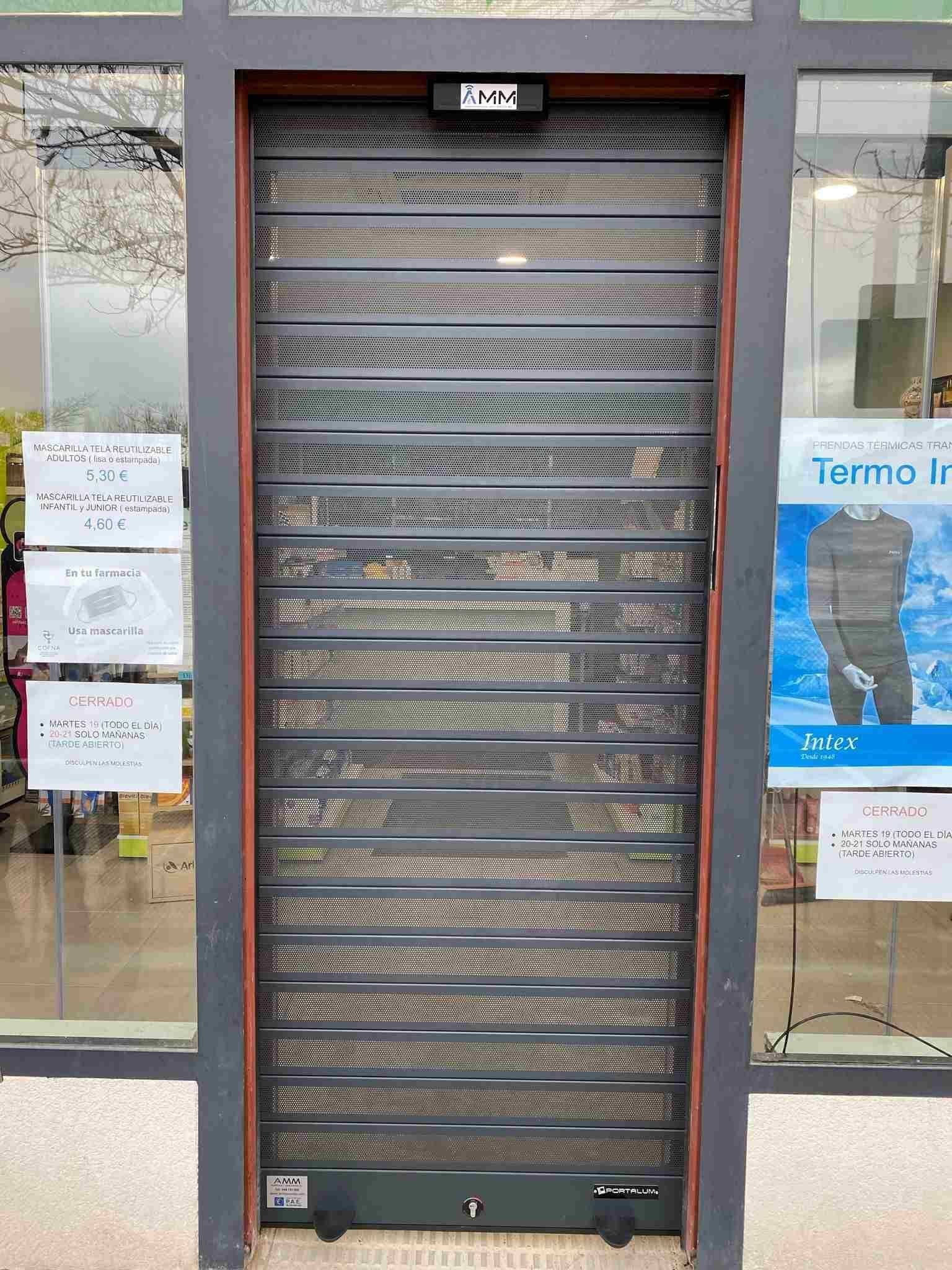 Un escaparate con una persiana cerrada y un cartel en ella.