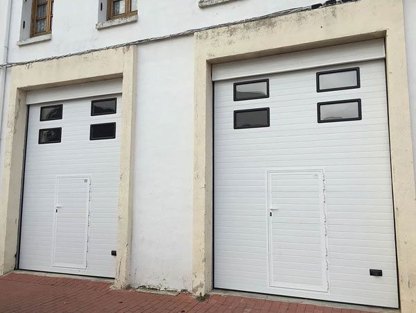 Dos puertas de garaje blancas están en el costado de un edificio.