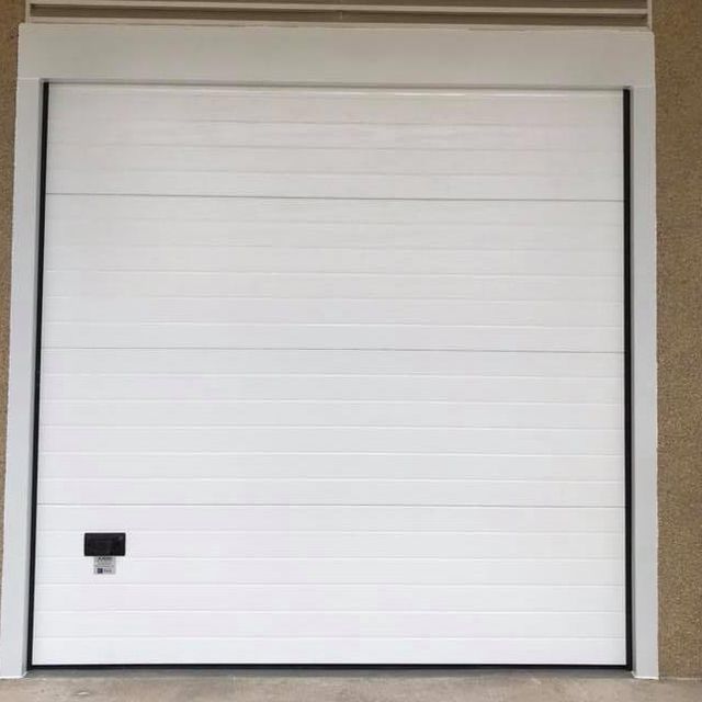 Una puerta de garaje blanca está encima de una pared marrón.