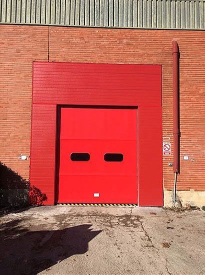 Una puerta de garaje roja está abierta frente a un edificio de ladrillo.
