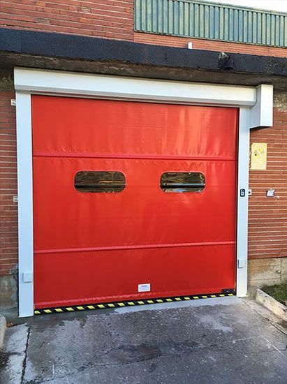 Una puerta de garaje roja está frente a un edificio de ladrillos.