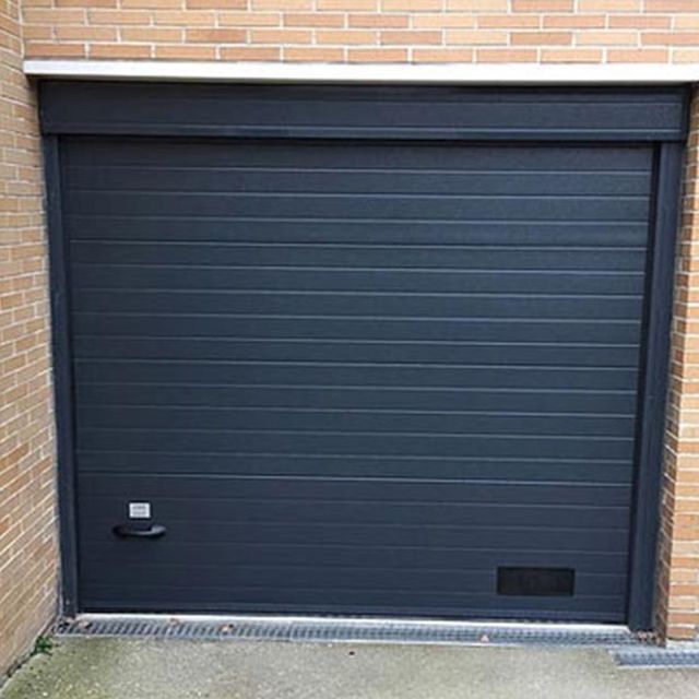 Una puerta de garaje negra está colocada al costado de un edificio de ladrillos.