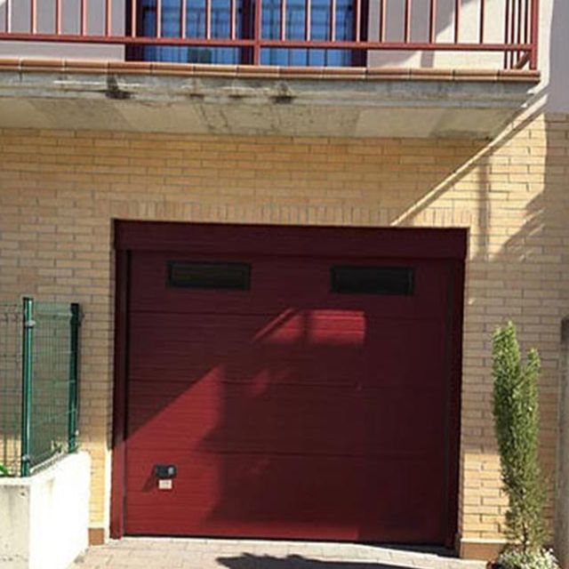 Una puerta de garaje roja está frente a un edificio de ladrillos.