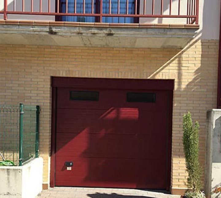Una puerta de garaje roja está frente a un edificio de ladrillos.