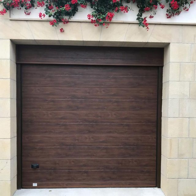 Una puerta de garaje marrón con flores rojas en el costado.
