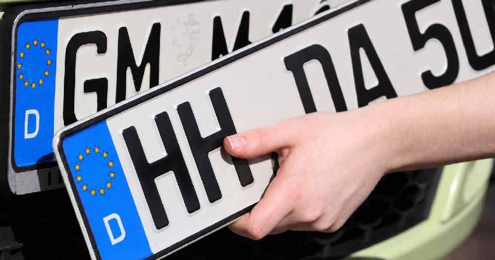 Hand tauscht ein schwarz-weißes europäisches Nummernschild an einem Auto aus