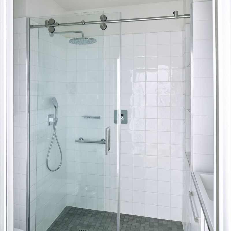 Glasduschkabine mit Schiebetür und Chromarmaturen in einem weiß gefliesten Badezimmer.