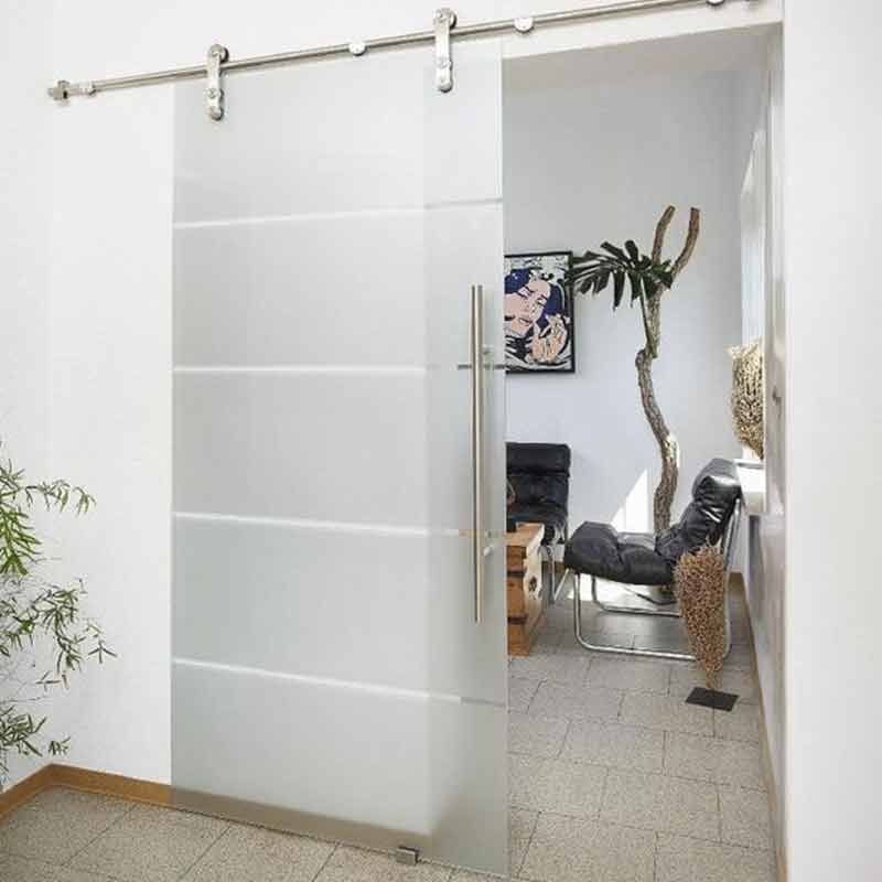 Schiebetür aus Glas mit mattierten horizontalen Paneelen und Edelstahlbeschlägen, die einen Raum mit Möbeln und einer Pflanze freigibt.