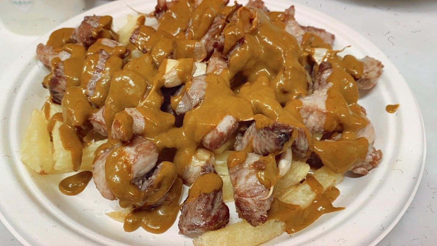 Un plato blanco cubierto con carne y papas fritas con salsa.