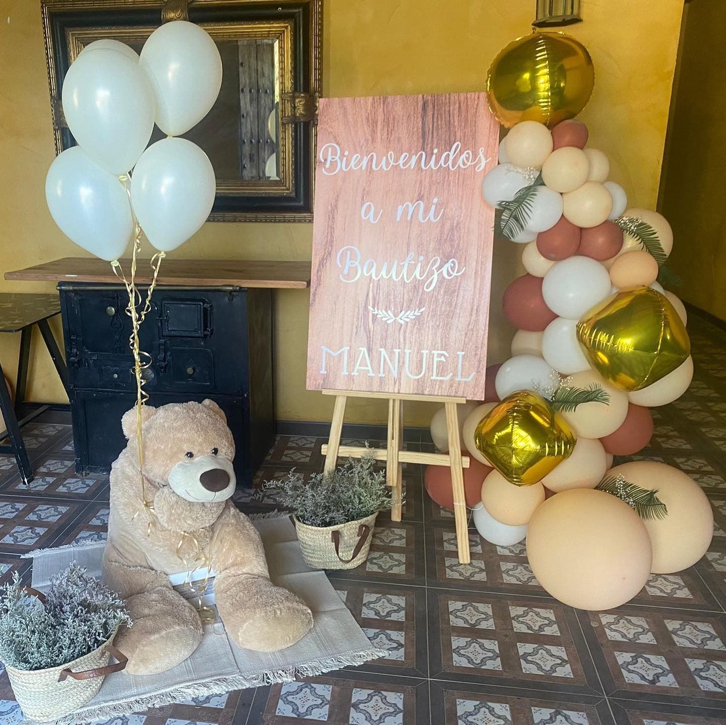 Un osito de peluche está sentado frente a un cartel que dice bienvenidos a mi bautizo manuel