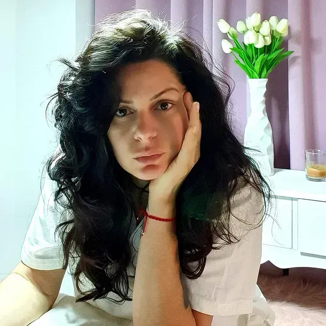 Una mujer con cabello largo está sentada en una mesa con la mano en la cara.