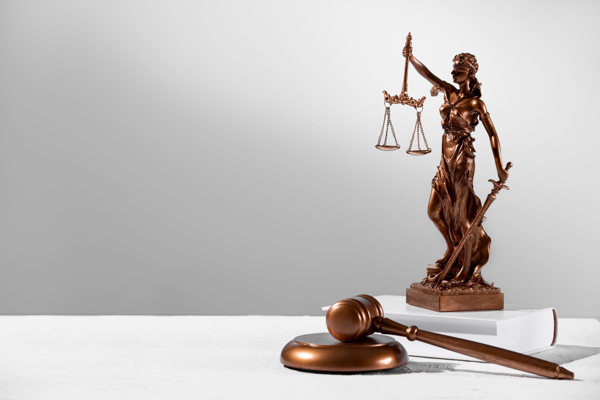 Una estatua de la justicia está sentada encima de un libro al lado del mazo de un juez.