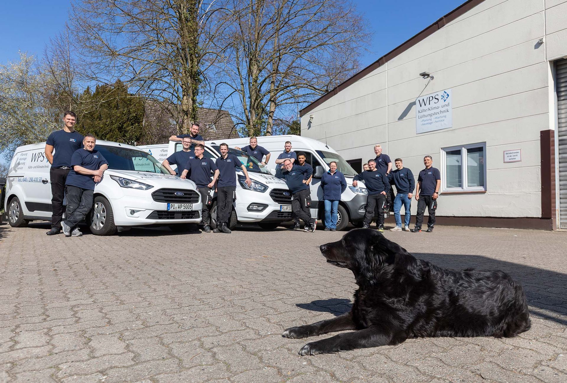 Die zuständigen Mitarbeiter für Klimatechnik in Hamburg und der Hund des Geschäftsführers stehen zwischen Transportern auf dem Hof von WPS. 