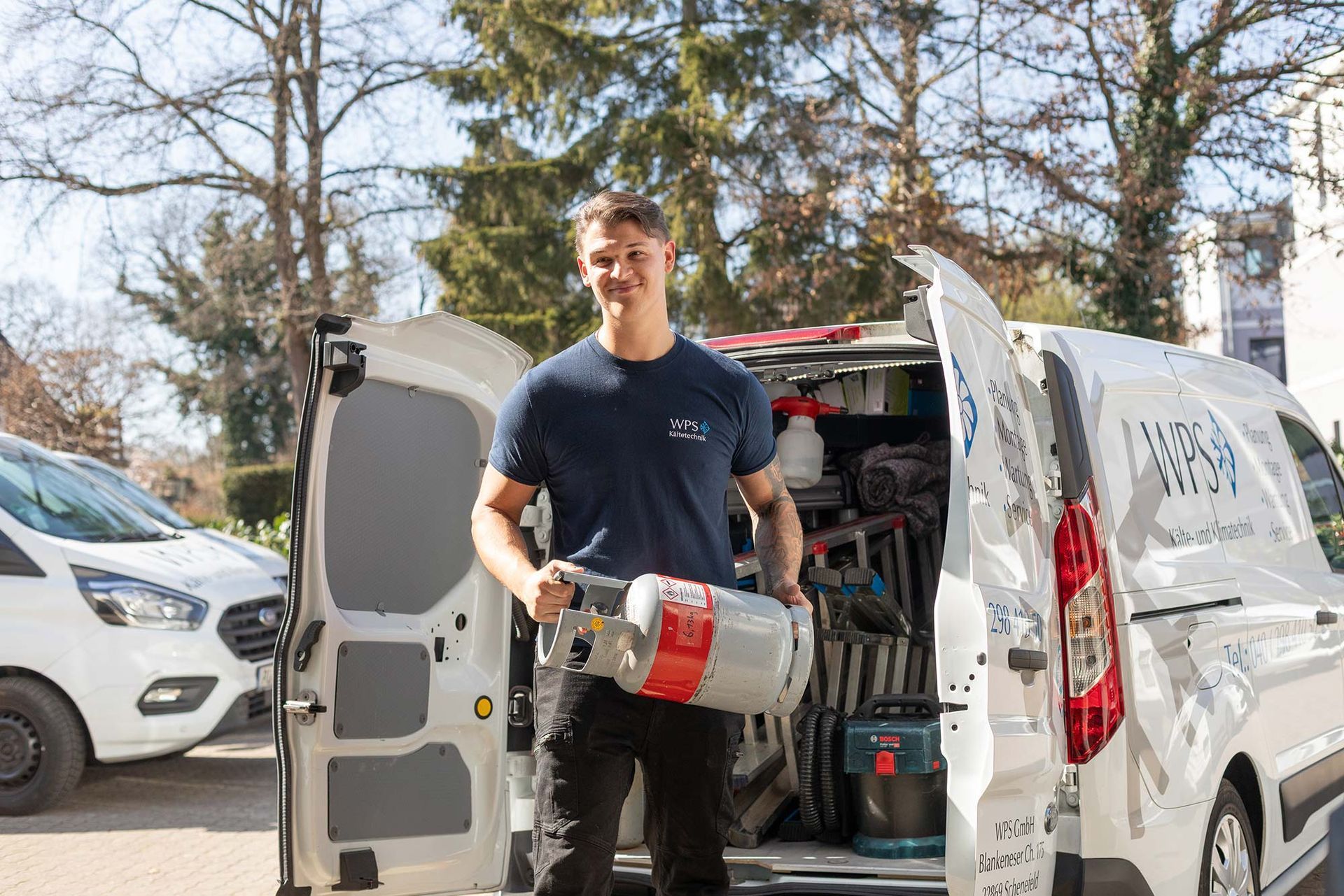 Ein Mann steht mit einem Werkzeug in der Hand vor einem Lieferwagen.