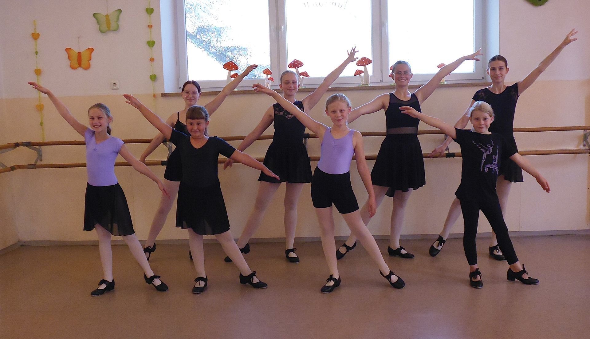 Die Beine und Füße der Tänzerinnen in schwarzen Ballettschuhen bilden einen Kreis auf dem Holzboden des Studios.