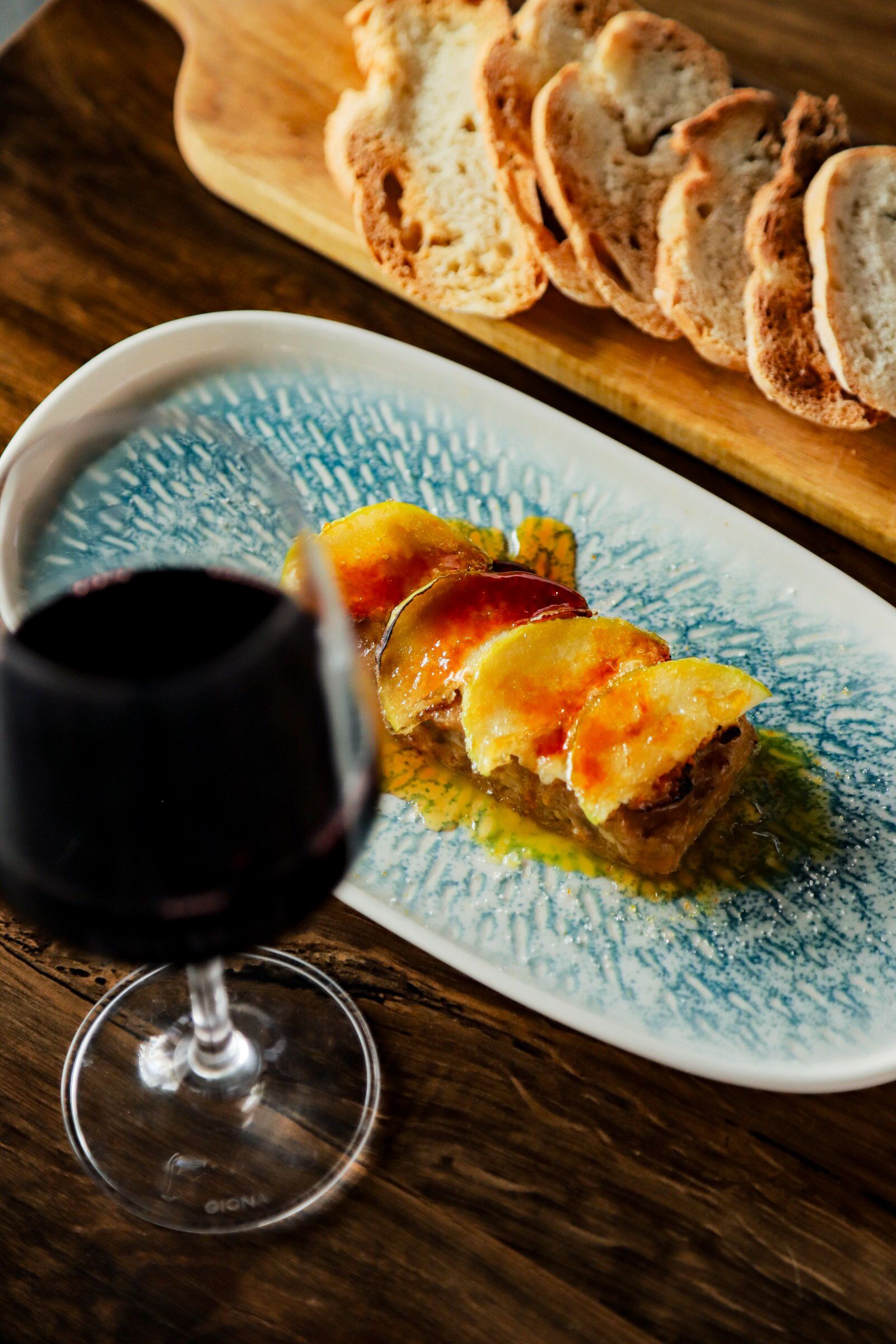 Un plato de comida y una copa de vino en una mesa de madera.
