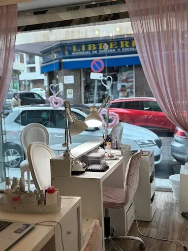 Pequeño salón de belleza con mesas y sillas para manicura, con vistas a la calle a través de grandes ventanales frontales.
