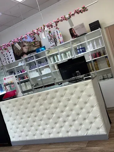 Mostrador de salón de manicura con frontal blanco acolchado, estantes de cristal y decoración floral rosa 
