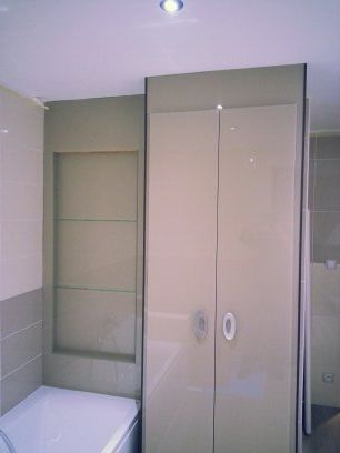 Petite salle de bains avec baignoire, étagère en verre et cabine de douche beige.