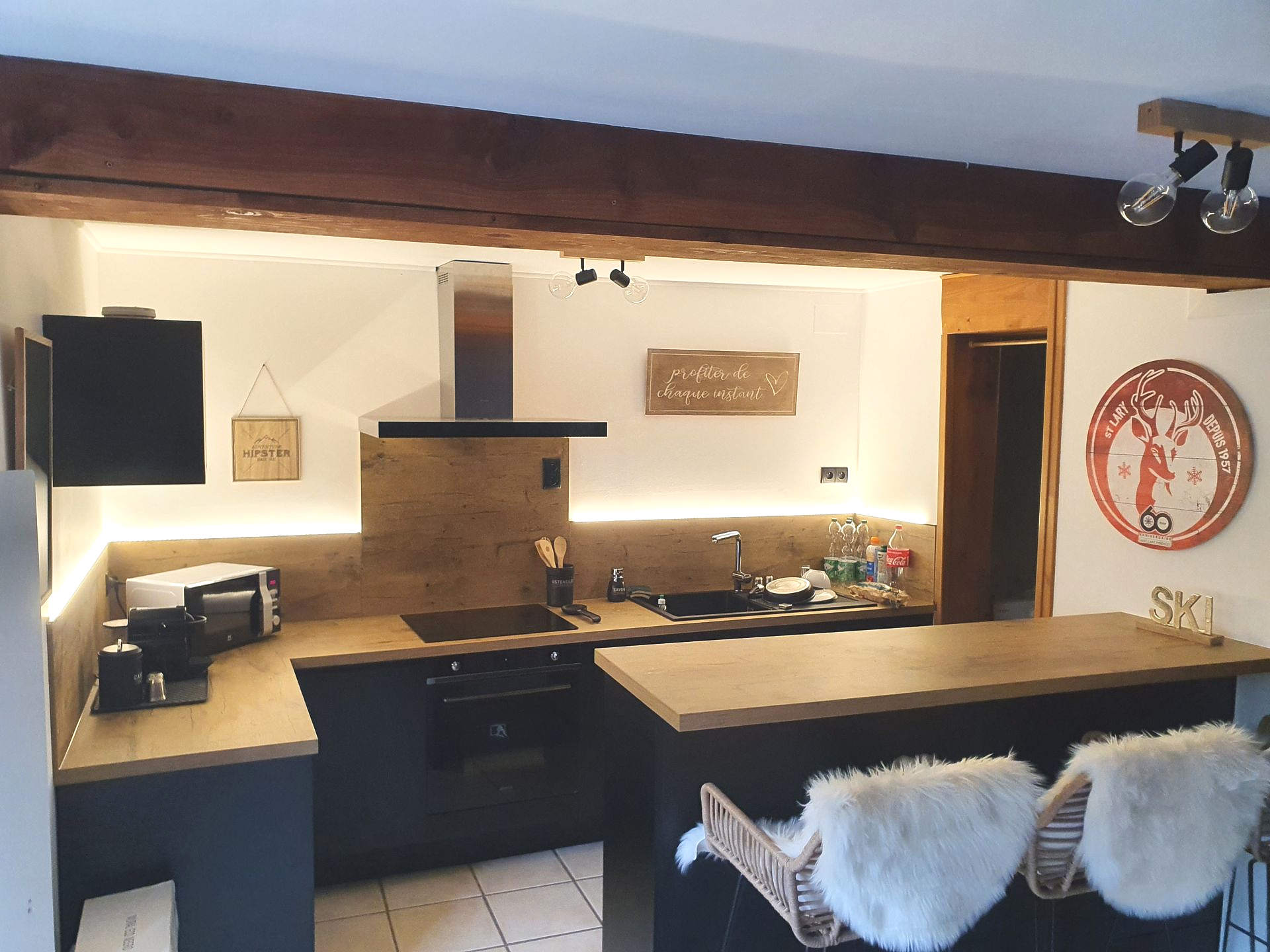 Cuisine moderne avec placards noirs, comptoirs en bois et un bar à petit-déjeuner avec deux tabourets en fourrure blanche.