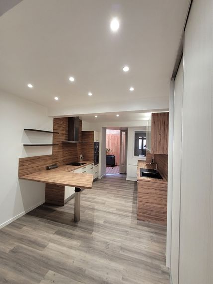 Cuisine moderne vide avec accents de briques, plafond blanc et parquet, vue depuis le salon