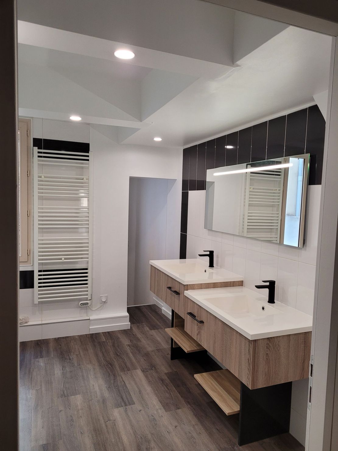 Salle de bains moderne avec double vasque, grand miroir, parquet foncé et murs blancs