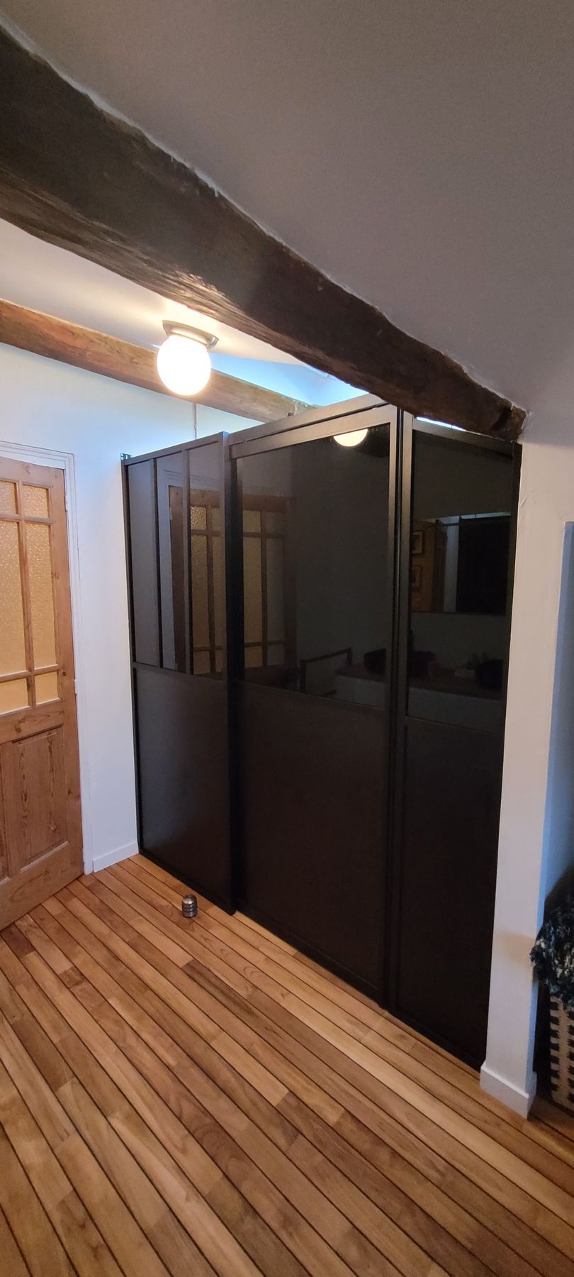 Couloir avec parquet, cloisons sombres, portes en bois et plafonnier.