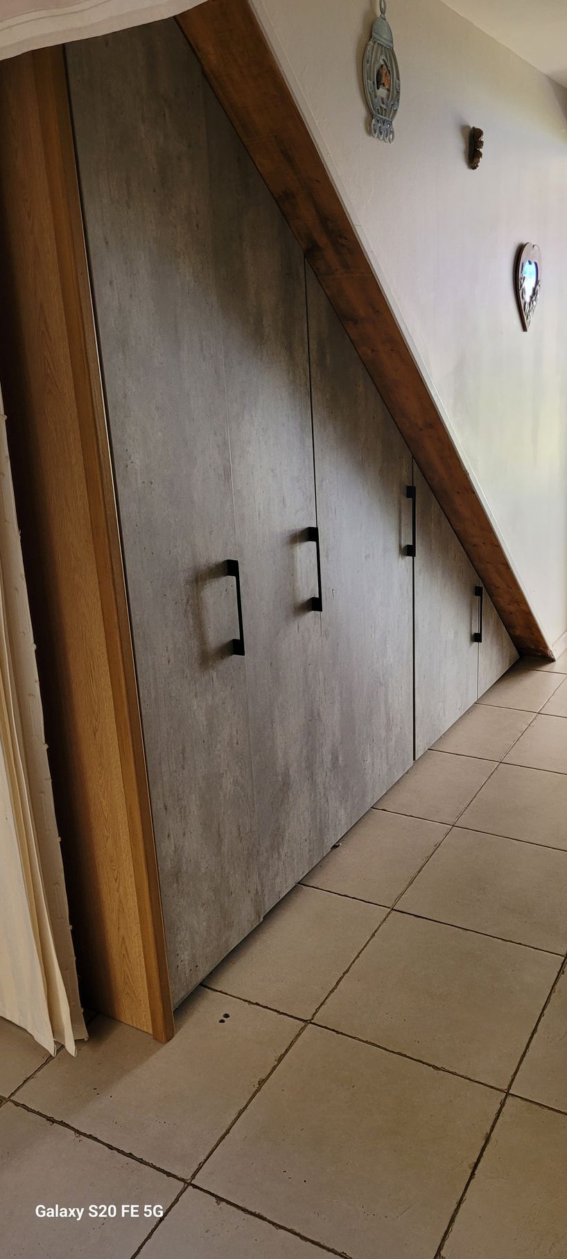 Portes de placard inclinées à panneaux de bois dans un couloir carrelé près d'une porte