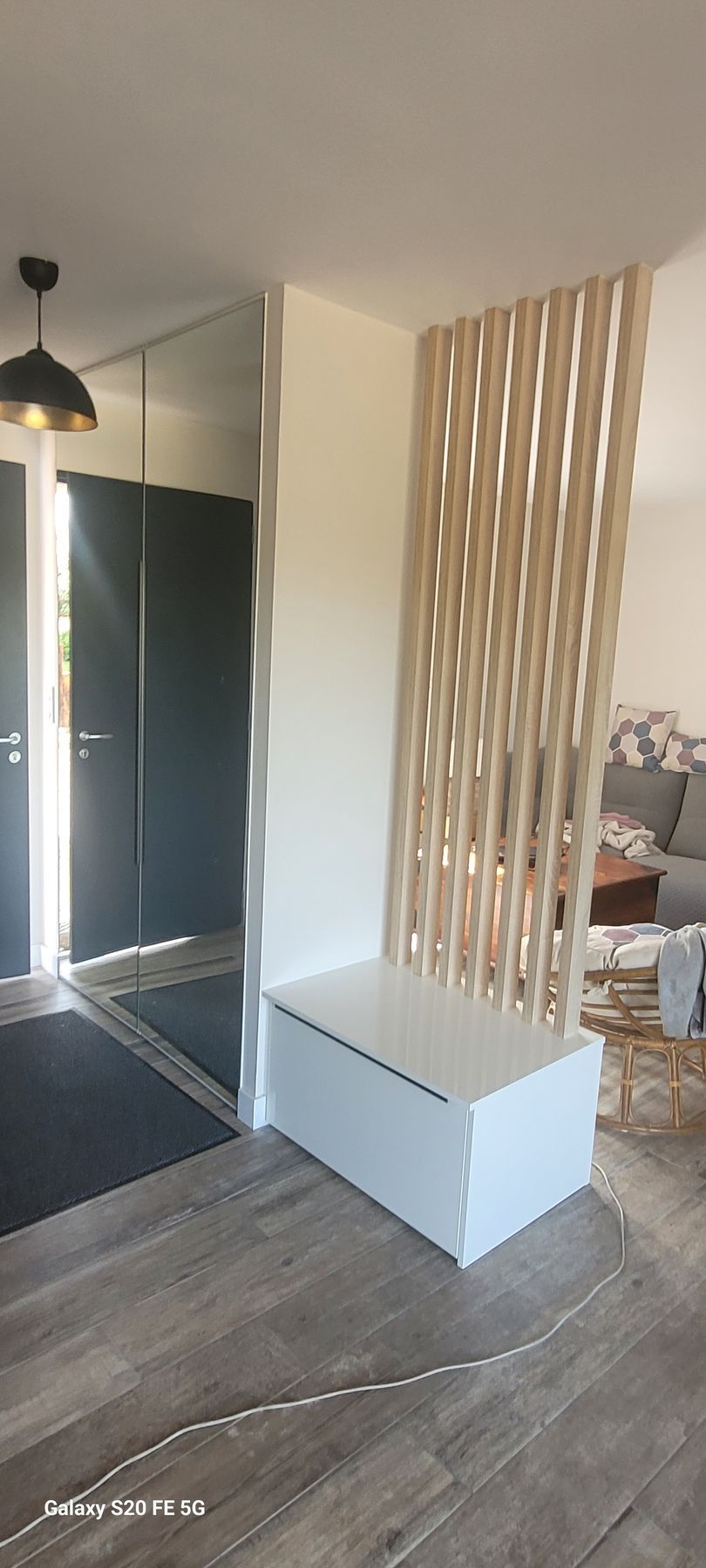 Entrée moderne avec placard à miroir, porte foncée, parquet, banc blanc et cloison verticale en lattes de bois.