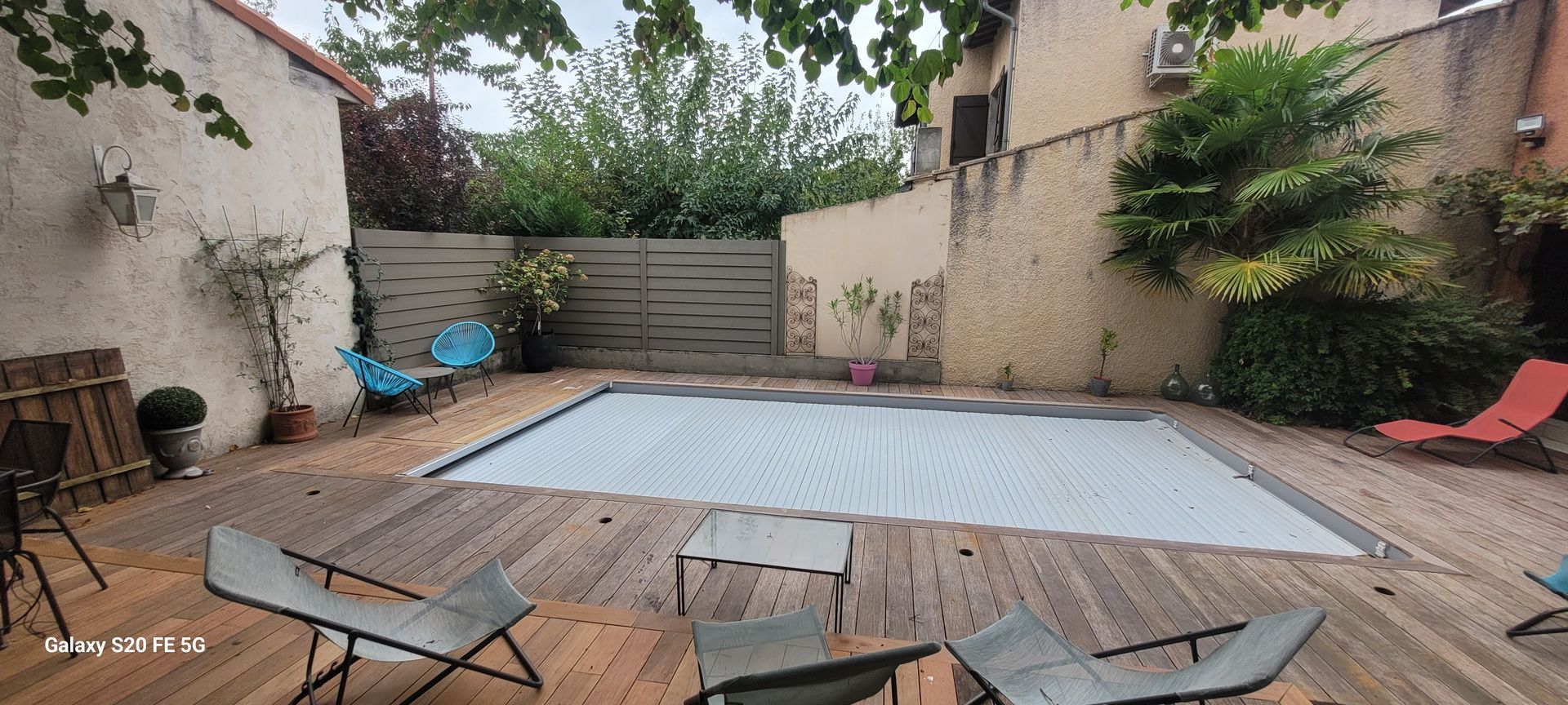 Terrasse arrière avec piscine couverte, chaises longues et sièges de jardin autour du patio.