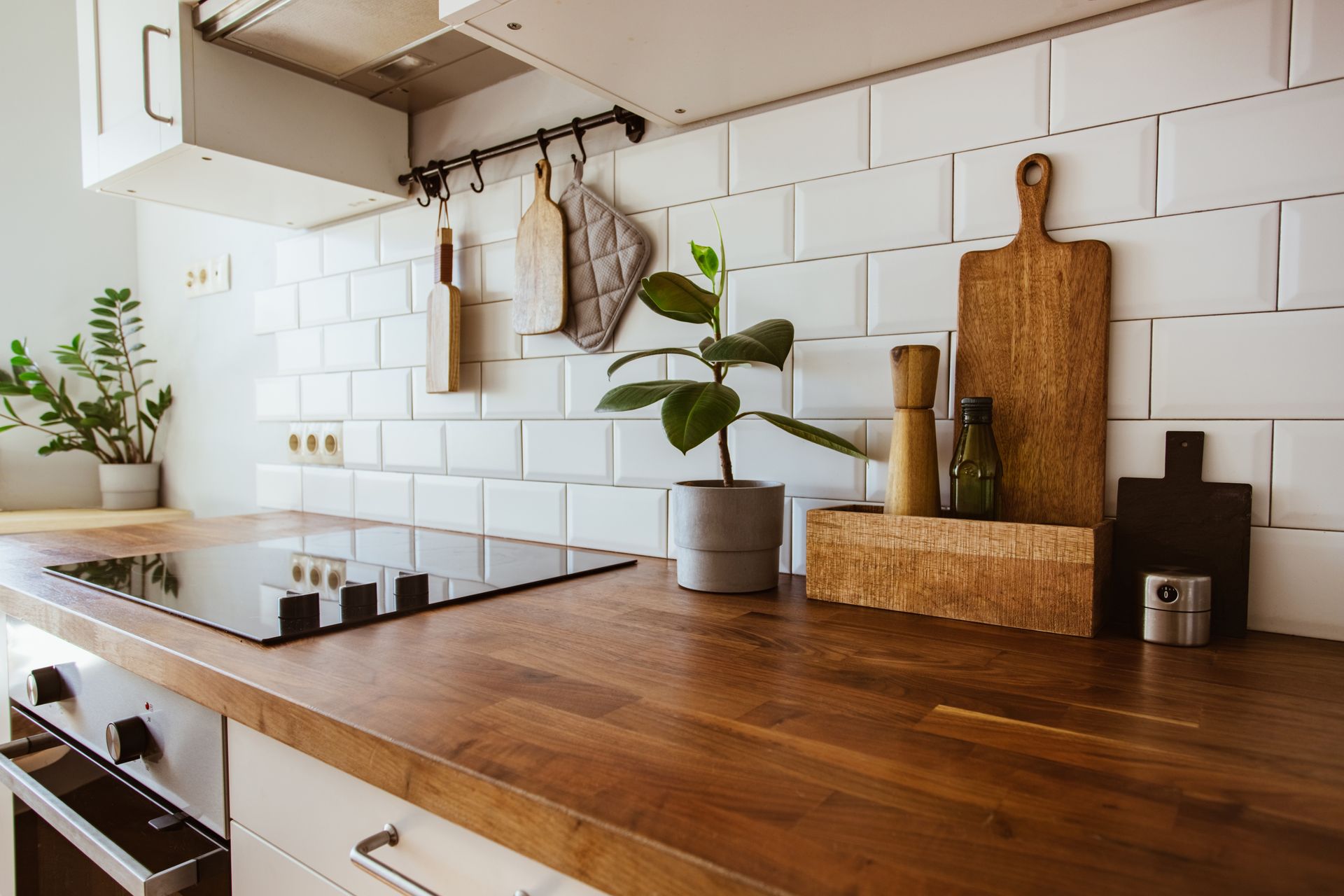 Plan de travail chaleureux avec crédence en carrelage blanc, planches à découper en bois, plante en pot et plaque de cuisson au gaz.