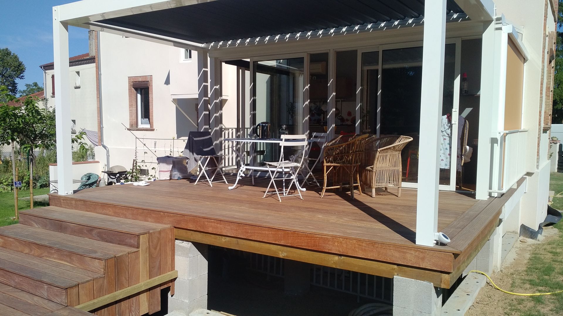Terrasse avec table à manger extérieure, chaises et pergola à côté d'une maison