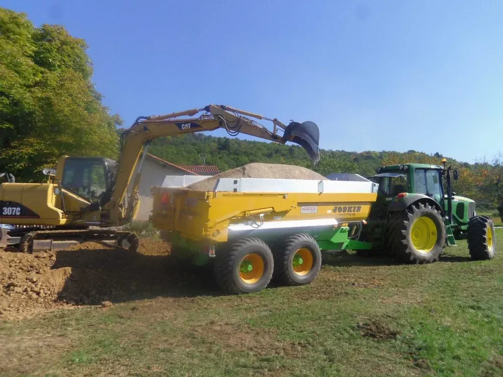Pelle mécanique hydraulique remplissant un camion-benne avec de la terre, assistée par un tracteur.