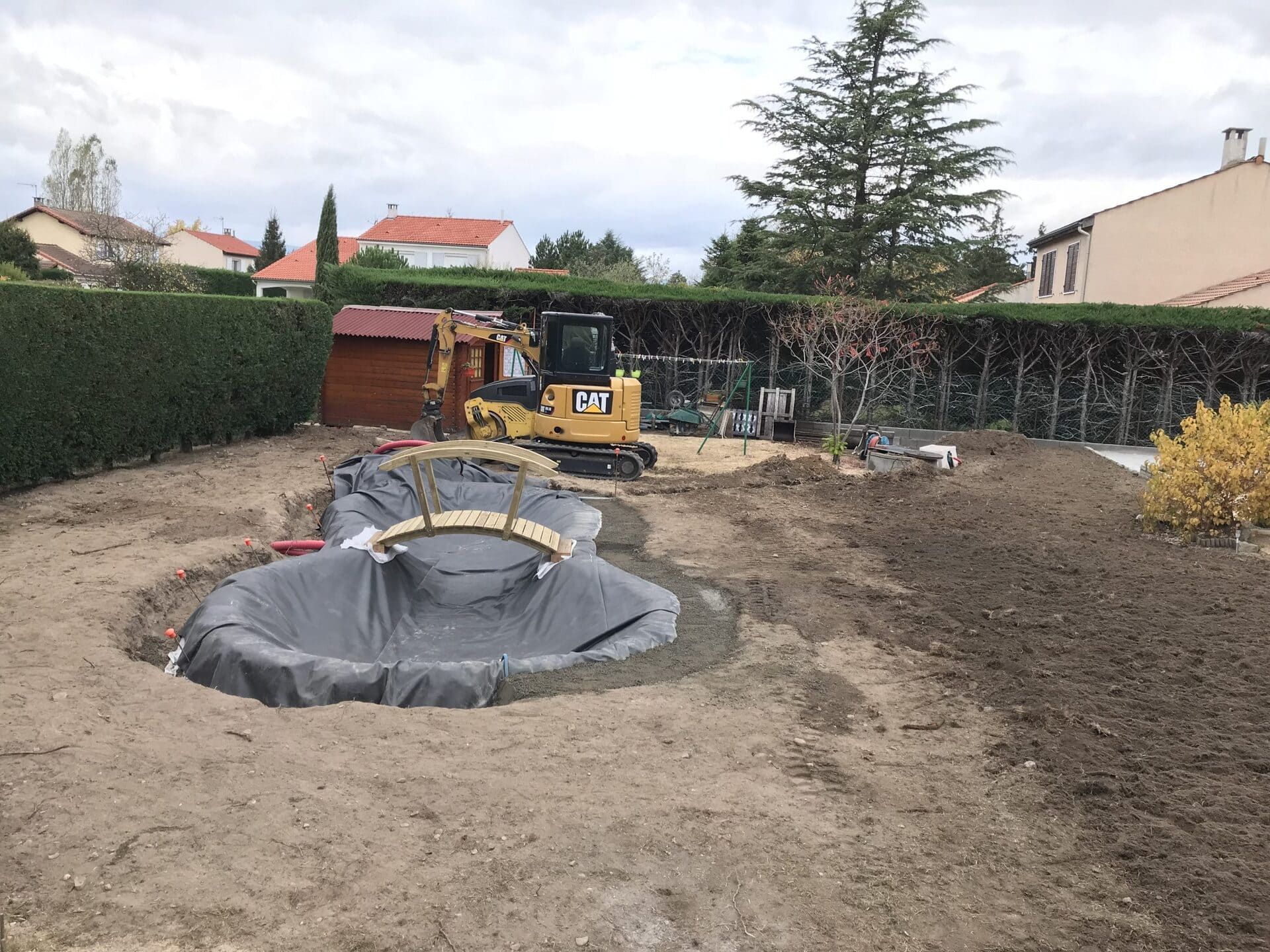 Chantier de construction d'un bassin avec une pelle mécanique et une bâche de protection sur le sol.