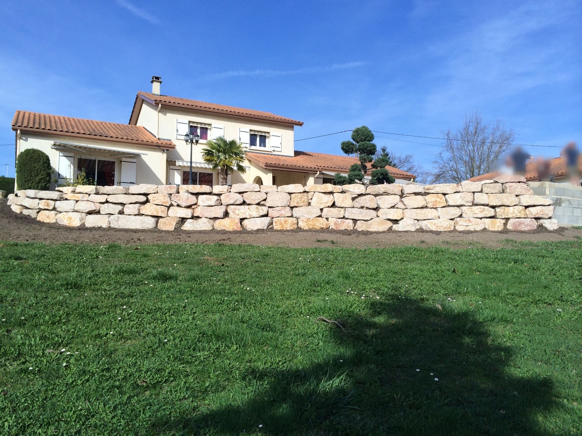 Création d'un grand mur en pierre naturel avec en arrière plan une maison sur deux étages.