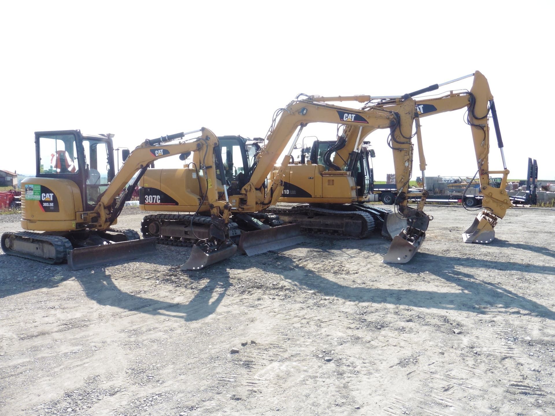 Trois pelles mécaniques Caterpillar alignées sur un chantier de construction, avec des modèles variés, y compris une mini-pelle et des excavatrices plus grandes.