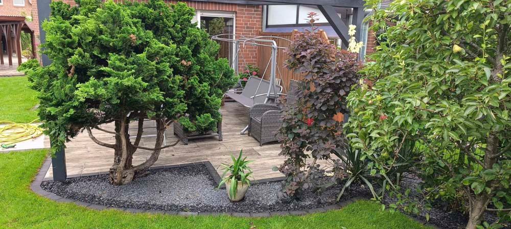 Der angelegte Hinterhof verfügt über eine Terrasse, verschiedene Sträucher und Bäume sowie einen Rasen. Die Anlage wirkt gepflegt.